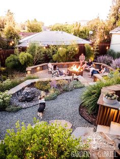 an outdoor fire pit surrounded by greenery and patio furniture with people sitting around it