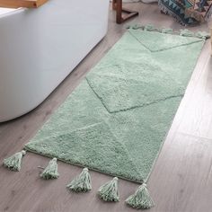 a green rug with tassels on the floor next to a bathtub in a bathroom