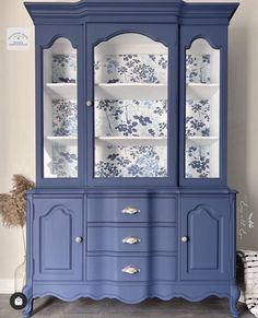 a blue china cabinet with glass doors and floral wallpaper on the front, in a room