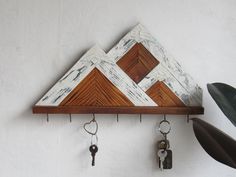 a wooden shelf with keys hanging from it's sides and a mountain design on the top