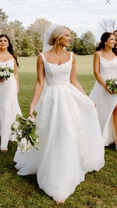 three brides walking in the grass with their bouquets and dresses pulled back to one side