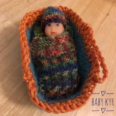 a knitted doll in a basket on a wooden floor with text overlay that reads, baby kyr