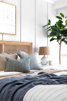 a bed with pillows, blankets and a potted plant on the headboard next to it