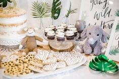 a table topped with cupcakes and cakes covered in frosting next to an elephant figurine