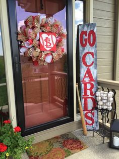 a red and white wreath sitting on the front door of a house next to a sign that says go cards