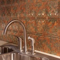 a stainless steel kitchen sink and faucet with decorative tiles on the wall behind it