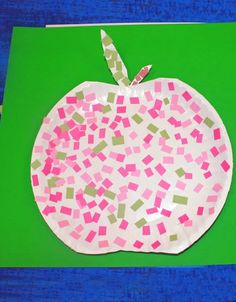 an apple shaped paper plate with pink and green squares in the center on a green mat