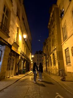 two people are walking down the street at night in an old european city with cobblestone streets