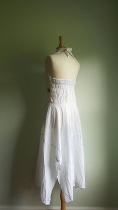 Embroidered sunflowers pop on this gorgeous white cotton-gauze dress. The lacy bodice flares into an ultra-full, handkerchief-hem skirt, with white satin ribbon accents. Easy fit, with a ruched, elasticized back and halter tie at neck. Best fits medium/large sizes. Era: 1970s Label: none ➸ visit on instagram | provenance_vintage White Cotton Maxi Dress With Lace Trim, Vintage White Sleeveless Sundress, White Sleeveless Vintage Sundress, White Flowy Sleeveless Halter Dress, White Lace Trim Maxi Dress For Festivals, White Sleeveless Sundress For Festival, White Halter Neck Sundress, White Cotton Sundress With Lace Trim, White Cotton Halter Neck Dress