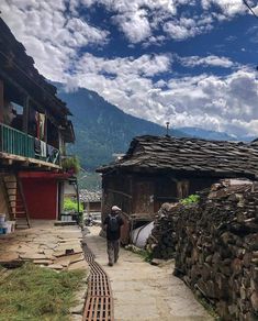 a man walking down a street next to a stone wall and building with mountains in the background