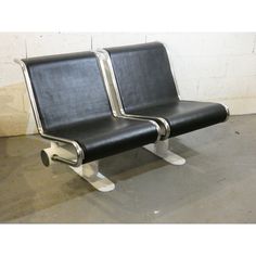 two black leather chairs sitting next to each other on top of a cement floor in front of a white brick wall