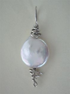 a large white pearl is hanging from a silver wire pendant on a white background with the word