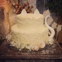 a cake with white frosting and flowers sitting on a table next to a cat figurine