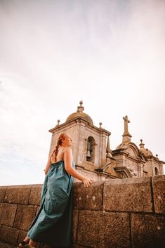 a woman in a blue dress leaning against a stone wall and looking up at the sky