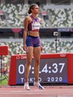 a woman standing on top of a track in front of a large stadium filled with people