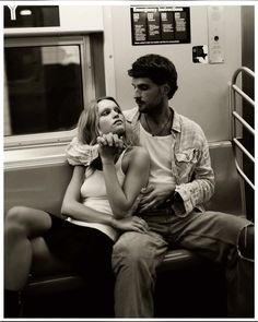 a man and woman sitting next to each other on a subway train, looking at each other