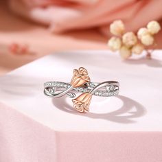 a rose shaped ring sitting on top of a white table next to a pink flower