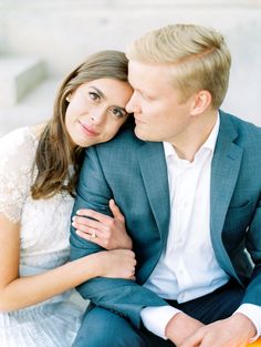 a man and woman sitting next to each other on a white couch with their arms around each other