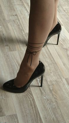 a woman's legs with a small tattoo on her left ankle, and black heels