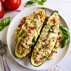 two zucchini boats on a white plate with basil and tomatoes in the background