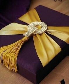 a gift wrapped in purple and gold ribbon with a diamond brooch on it's side