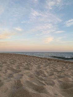 the beach is covered with sand and waves as the sun sets over the ocean in the distance