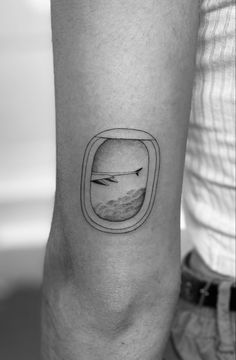 a black and white photo of an airplane window tattoo on the right arm, with clouds in the distance