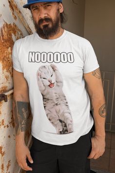 a man with a beard wearing a white t - shirt and black pants standing next to a rusted wall