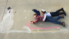 two children laying on the ground next to a chalk drawing of a snowman and a penguin