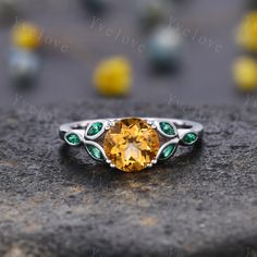 a ring with an orange stone surrounded by green and white stones on top of a rock