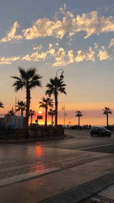 the sun is setting behind palm trees on the side of the road in front of the ocean