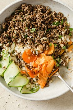 a white bowl filled with rice, meat and veggies on top of a table