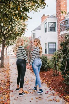 two women are walking down the sidewalk in front of some trees with leaves on them