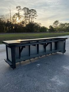 an empty bench sitting in the middle of a parking lot with trees and grass behind it