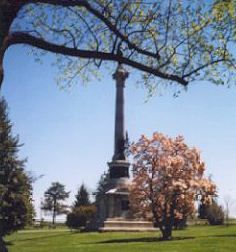 a monument in the middle of a park with trees and grass on either side of it