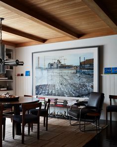 a dining room table and chairs in front of a large painting on the wall above it