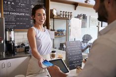 a woman standing at a counter with a tablet in front of her and a man behind the counter