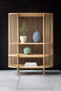 a bamboo shelf with two vases and a plant on top, against a black wall