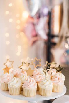 cupcakes with pink frosting and gold stars are on a white cake plate