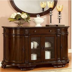 a large mirror on top of a wooden cabinet next to a vase and two candles