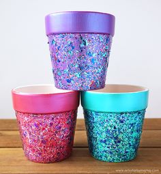 three colorful cups sitting on top of a wooden table covered in confetti sprinkles