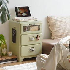 a woman sitting on the floor in front of a green filing cabinet next to a couch