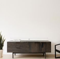 the sideboard is next to a potted plant in front of a white wall