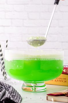 a green liquid in a bowl with a spoon and some books on the table next to it