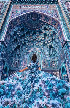 a woman is standing in front of an intricately decorated building with blue and pink flowers