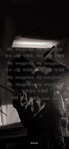 black and white photograph of man playing guitar in dark room with words written on wall