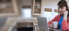 a woman sitting at a kitchen counter with a laptop and coffee mug in front of her