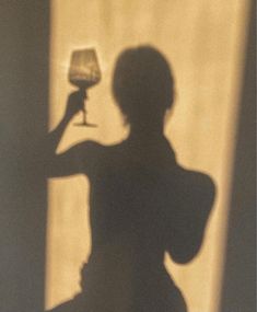 the shadow of a woman holding a wine glass in front of her face and arm