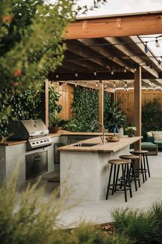 an outdoor kitchen with bar stools next to the grill and seating area, surrounded by greenery