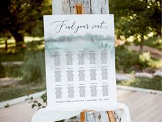 an easel with a wedding seating chart on it sitting in front of a tree